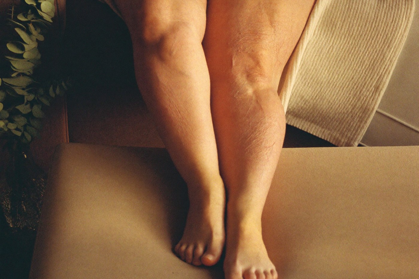 Jambes féminines au repos sur un canapé, chevilles fines et pieds épargnés, caractéristiques du lipœdème, dans une lumière douce